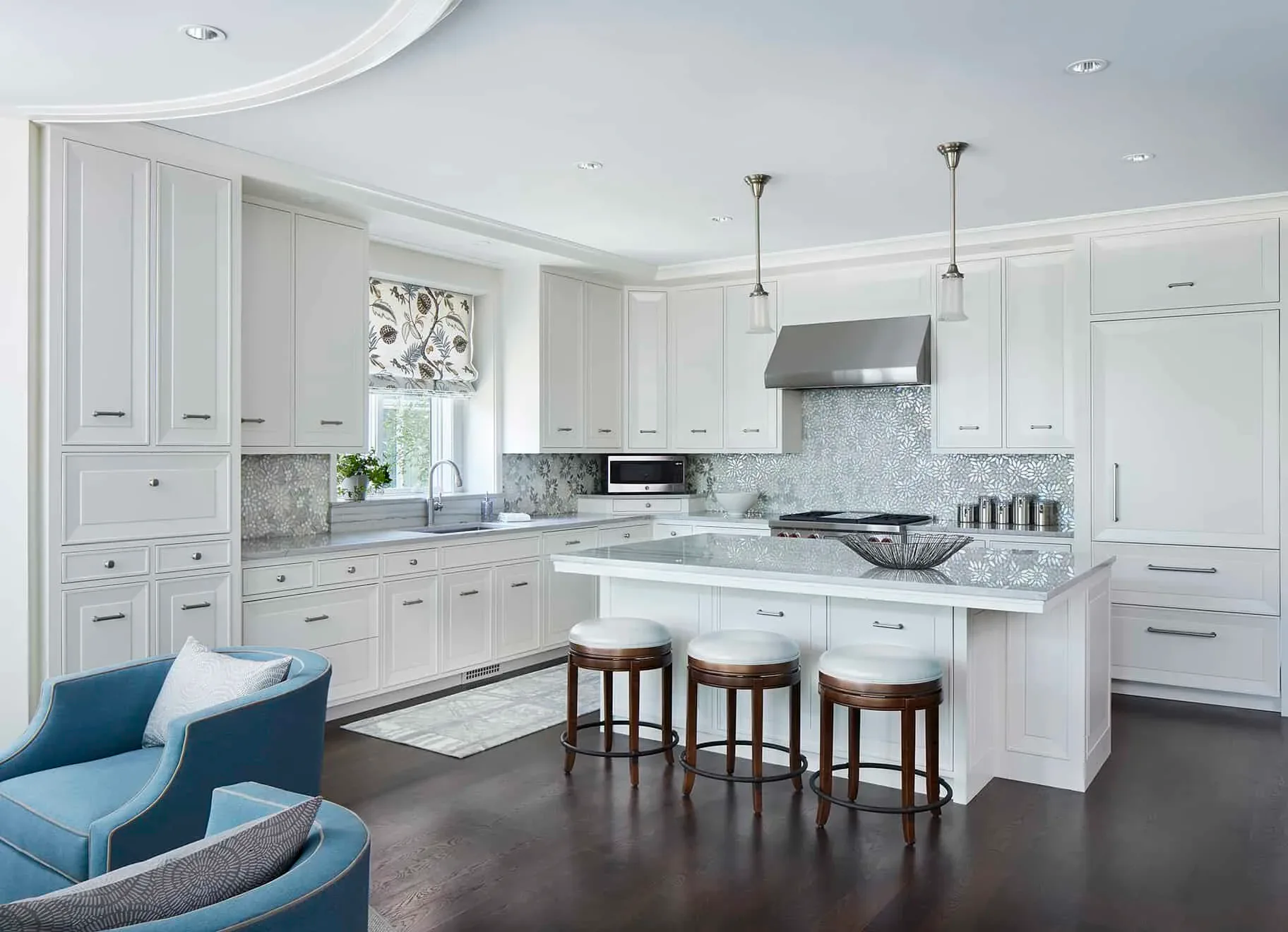 Modern white kitchen with marble island, gray subway tile backsplash, stainless steel appliances, and dark hardwood floors, designed by Pamela R Ackerman.
