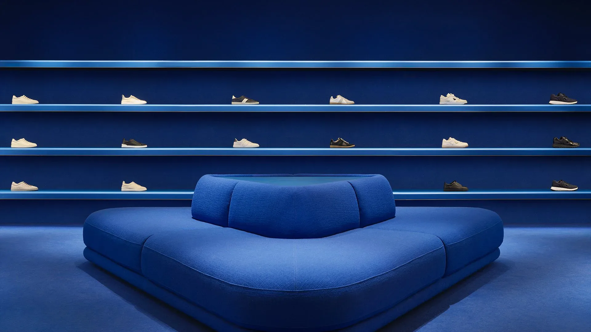 Blue minimalist interior with sculptural curved seating element and shoe display shelving on walls, by Paolo Ferrari.