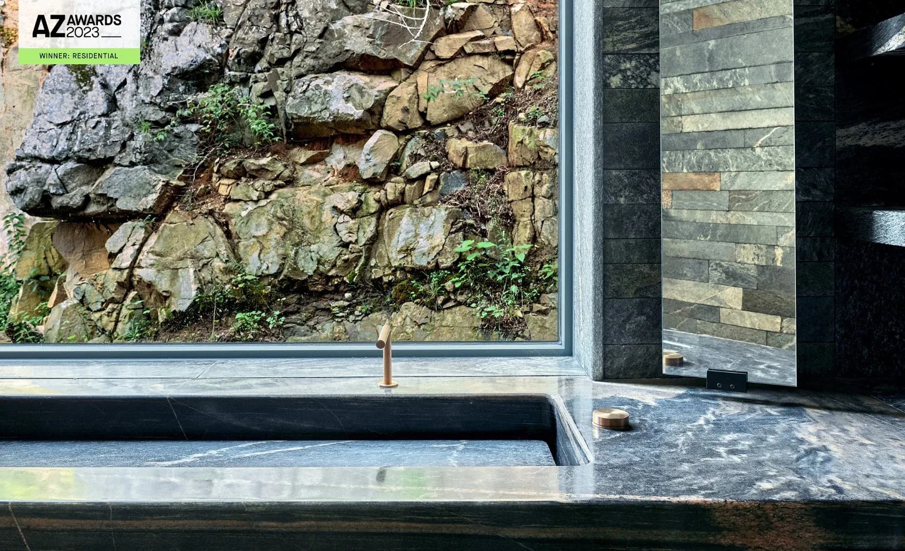 Modern architectural detail showing natural stone wall integration with contemporary framing and dark stone cladding, designed by Paolo Ferrari.