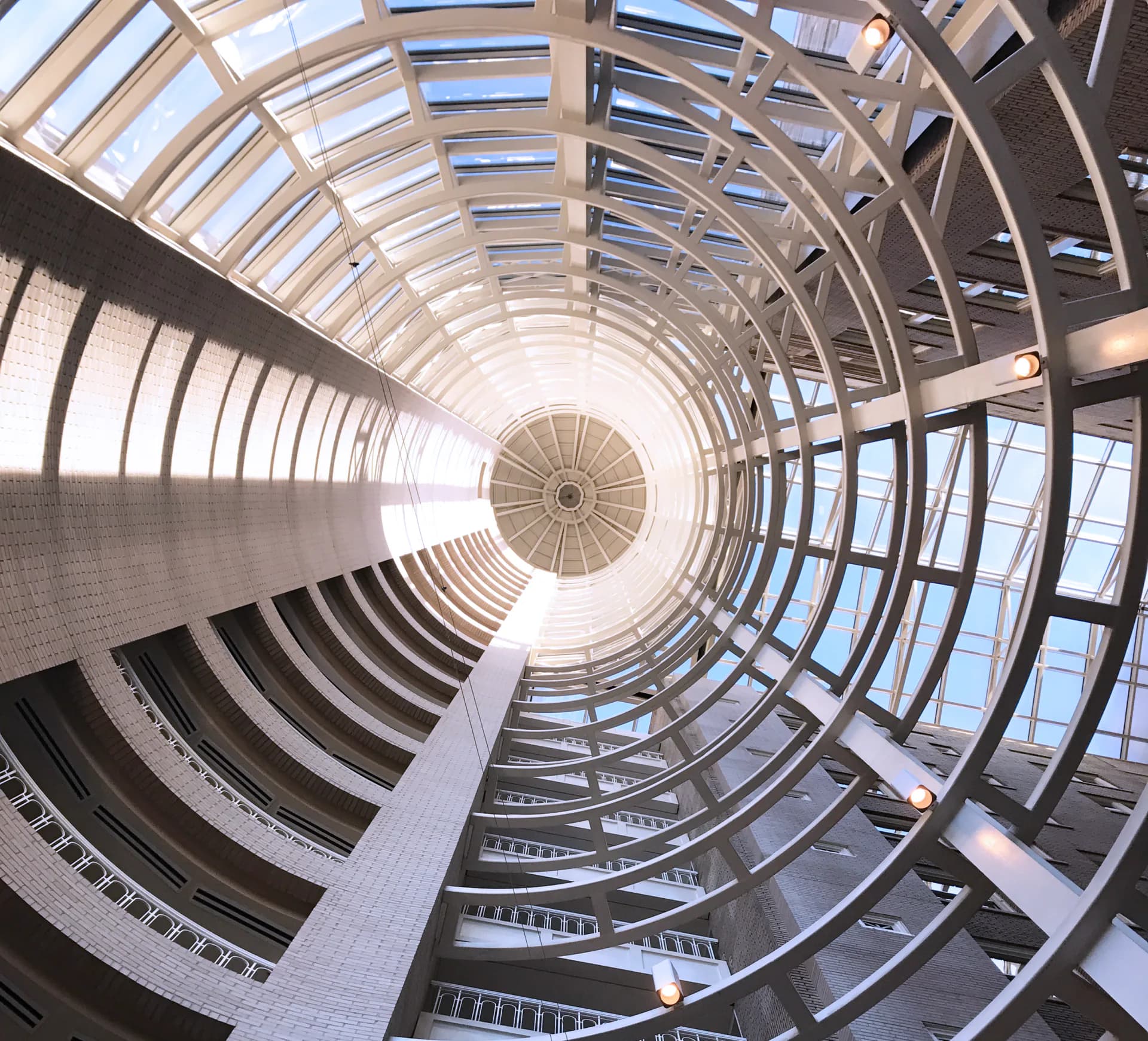 Spiral atrium with curved balconies and skylights creating a dramatic upward perspective, featuring modern architecture with glass and metal elements by Parker Cutler.