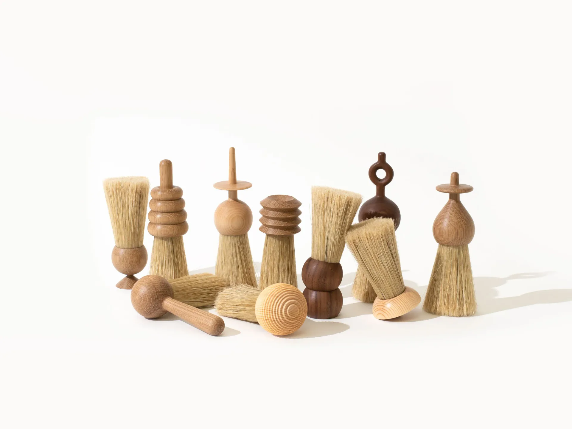 Wooden craft objects and utensils including brushes, beaters, and decorative forms arranged on white surface by Pat Kim.