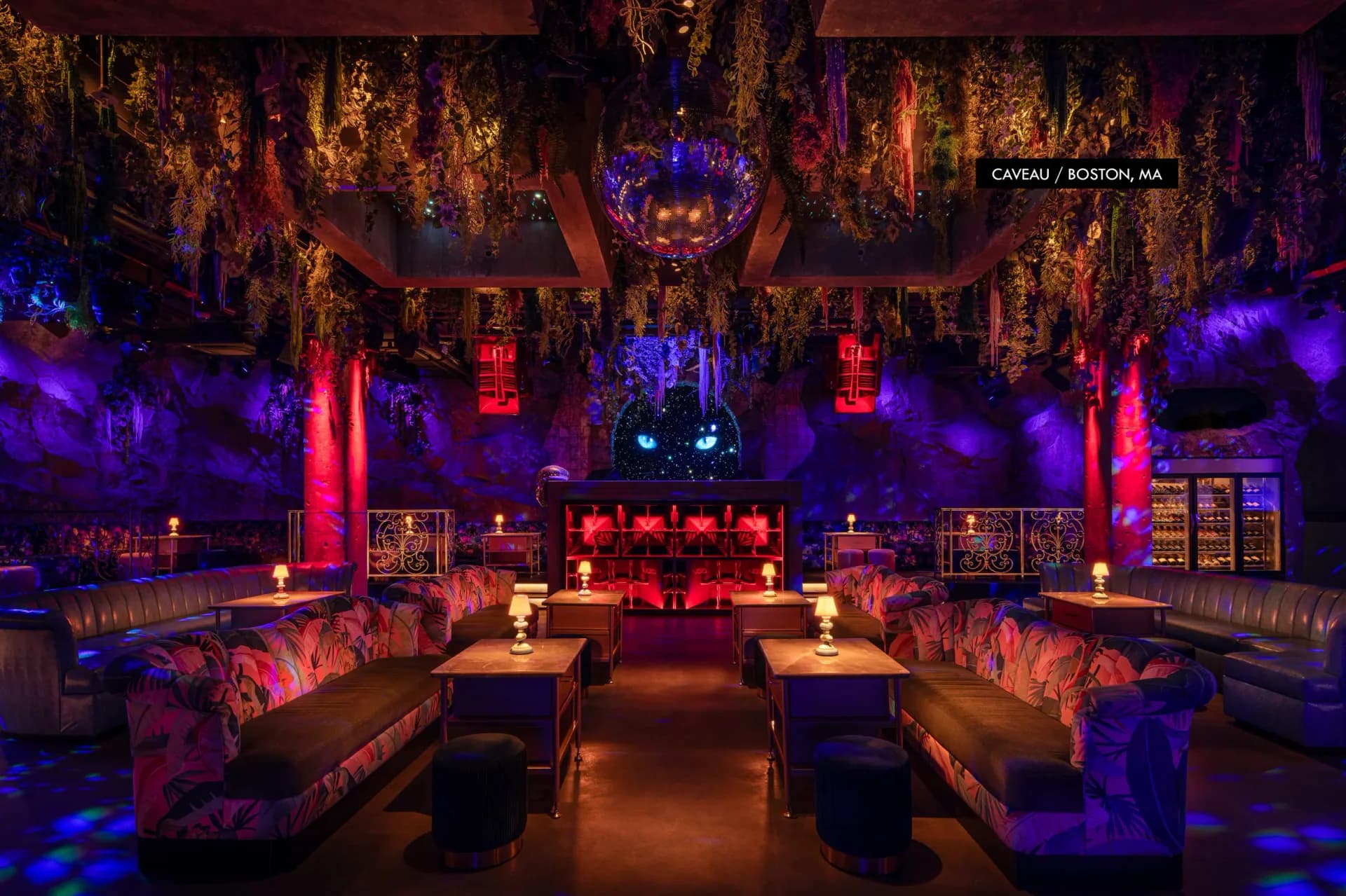Luxurious nightclub interior with purple and red ambient lighting, ornate gold ceiling details, pink patterned banquettes, and dramatic architectural elements by Paul Gregory.