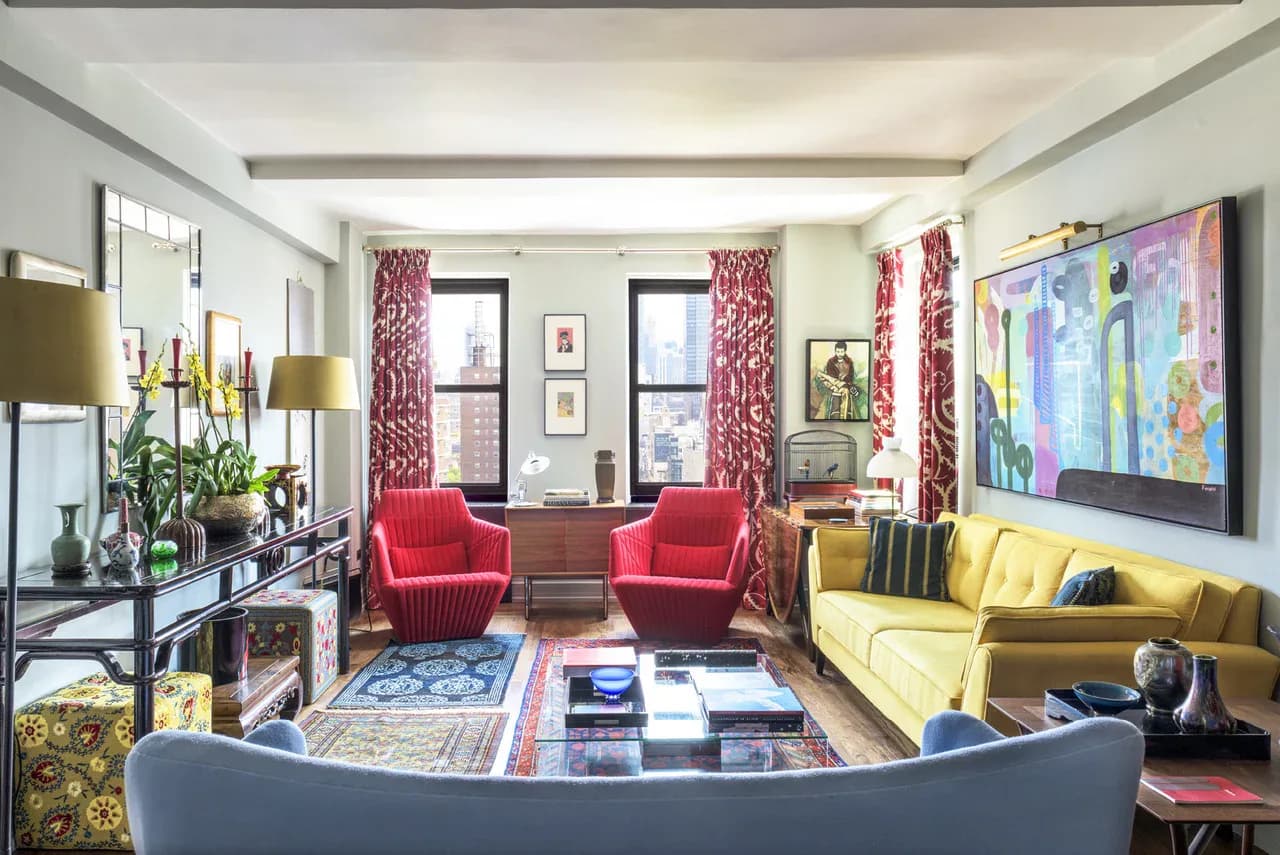Elegant living room with red velvet chairs, yellow sofa, patterned curtains, and colorful artwork, designed by Perry Sayles.