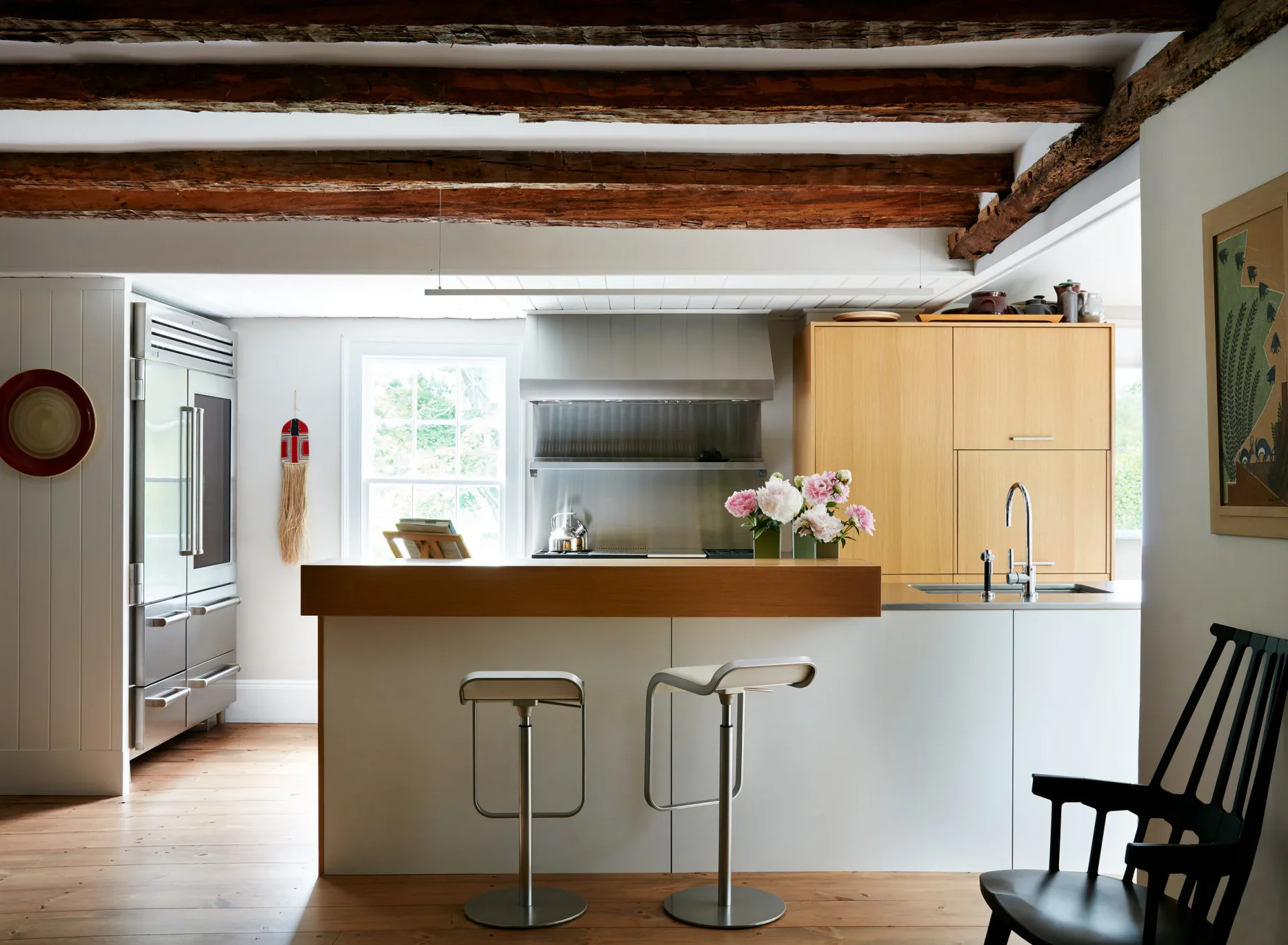 Modern kitchen with white cabinetry, wood-topped island with chrome stools, exposed timber ceiling beams, and stainless steel appliances by Perry Sayles.