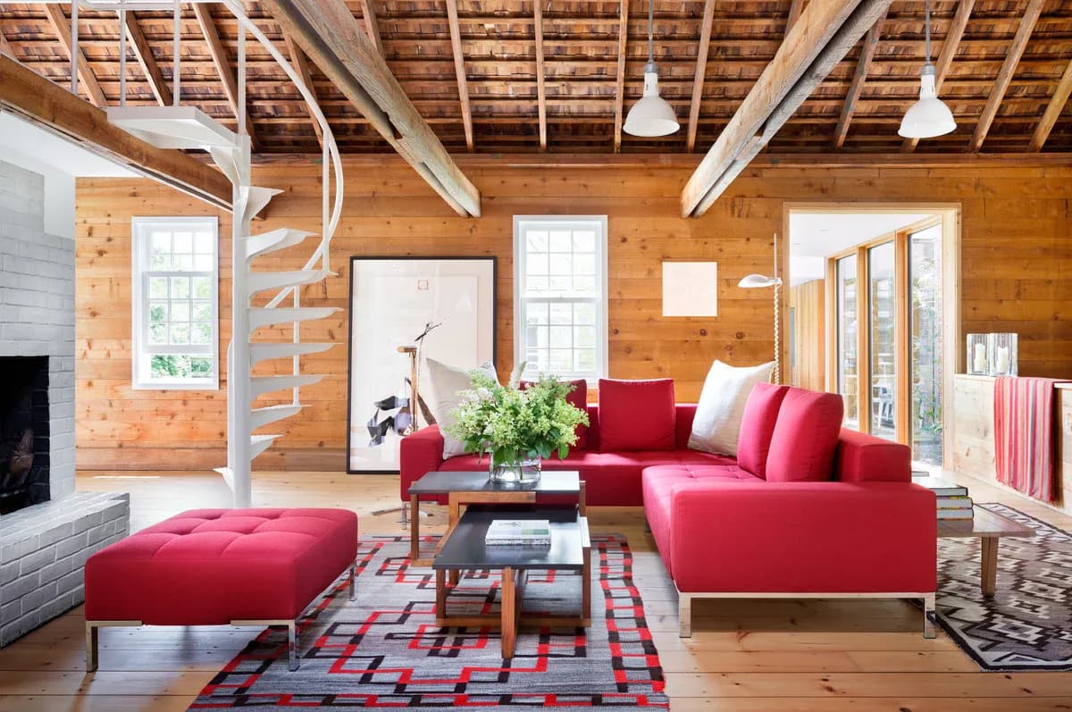 Bright wood-beamed living room with red and pink sectional seating, geometric area rug, and modern pendant lighting by Perry Sayles.