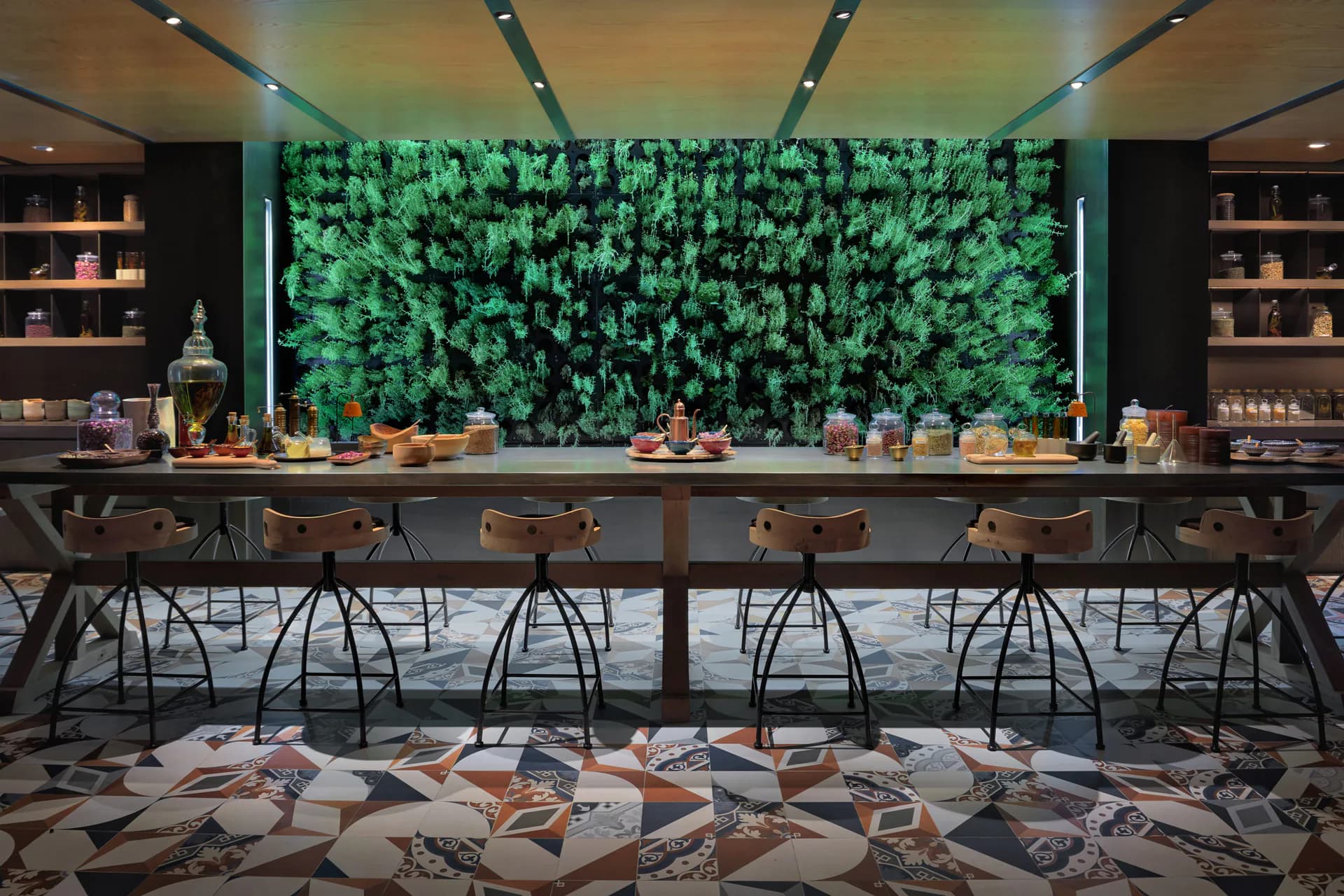 Modern bar interior with living green wall backdrop, dark shelving, wood countertop, contemporary seating, and geometric floor pattern by Peter O'Kennedy.