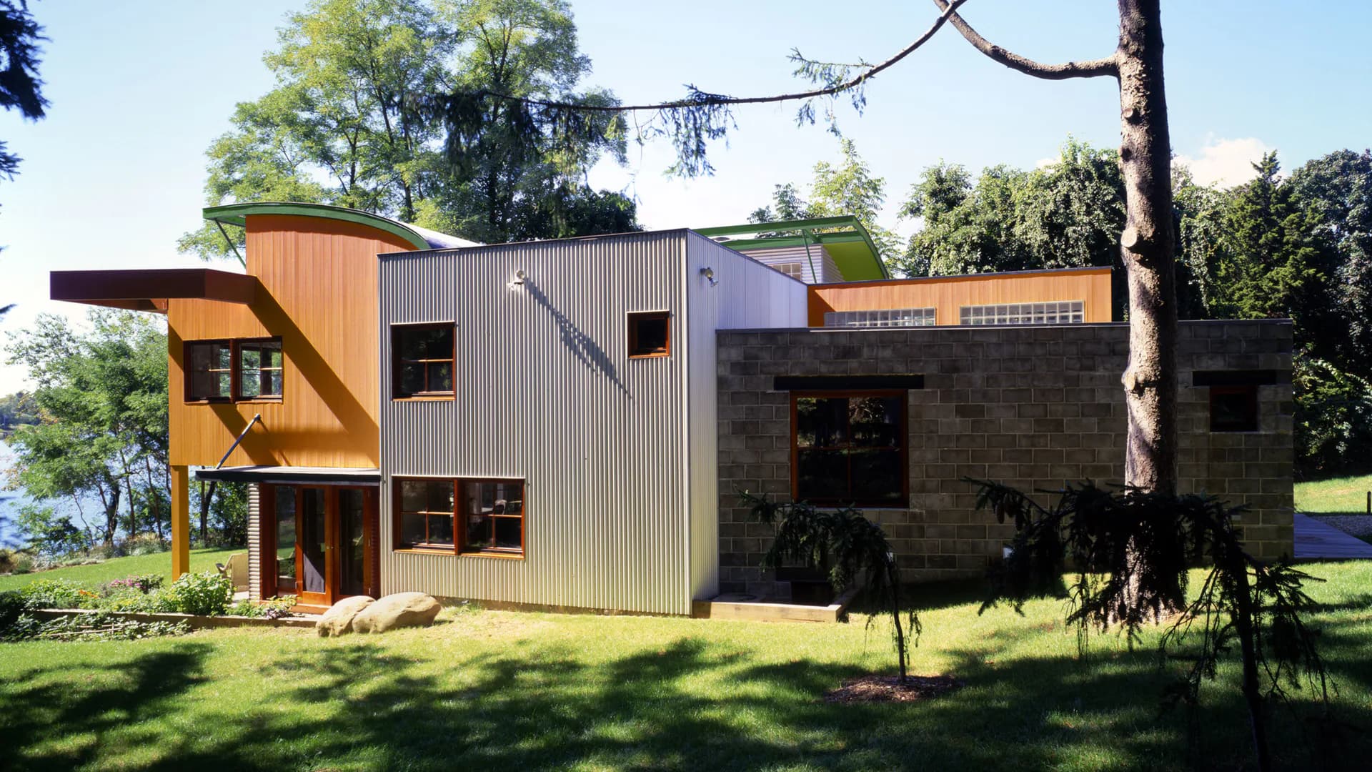 Modern residential architecture featuring angular copper and corrugated metal cladding with stone elements, set in a pastoral landscape with mature trees, by Peter Stamberg.