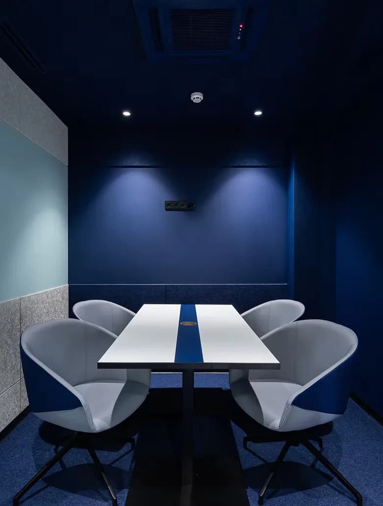 Modern conference room with deep navy walls, white table with blue accent stripe, sculptural white chairs, and recessed lighting by Prosha Korangy.