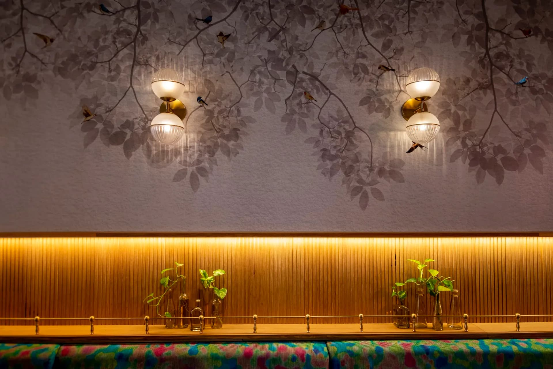 Modern interior with warm golden ribbed wall paneling, pendant lighting with botanical elements, and decorative leaf motifs on ceiling by Prutha Raithatha.
