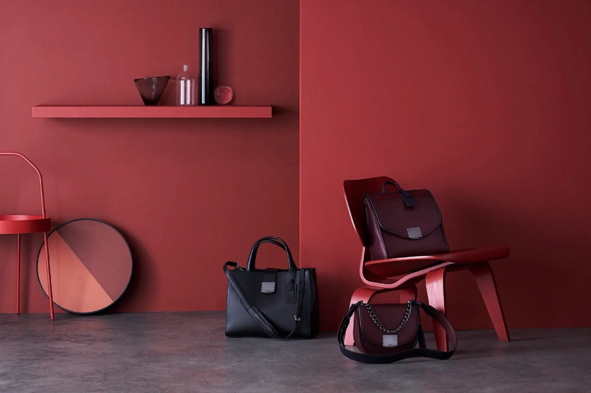 Monochromatic burgundy interior featuring a floating shelf, modern chair, handbags, and decorative accessories against a deep red wall by Quin Nichols.