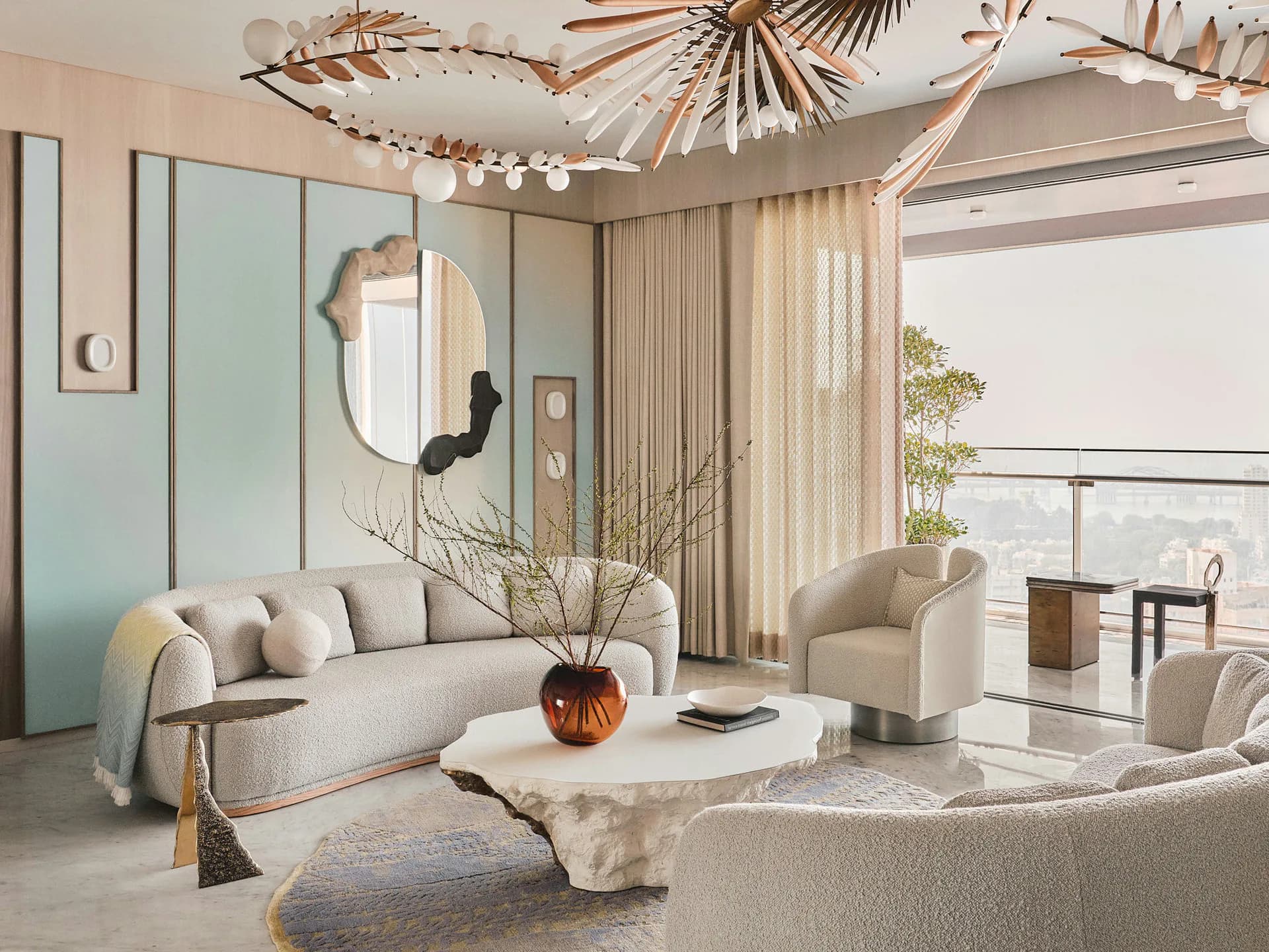 Luxurious modern living room with curved cream sofa, sculptural lighting fixture, and floor-to-ceiling windows overlooking a balcony by Rachel Cope.