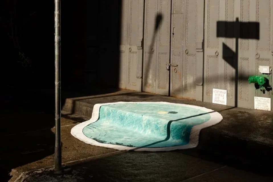 Turquoise sculptural pool installation in industrial concrete space with metal doors and green plant accent by Rafael Prieto.
