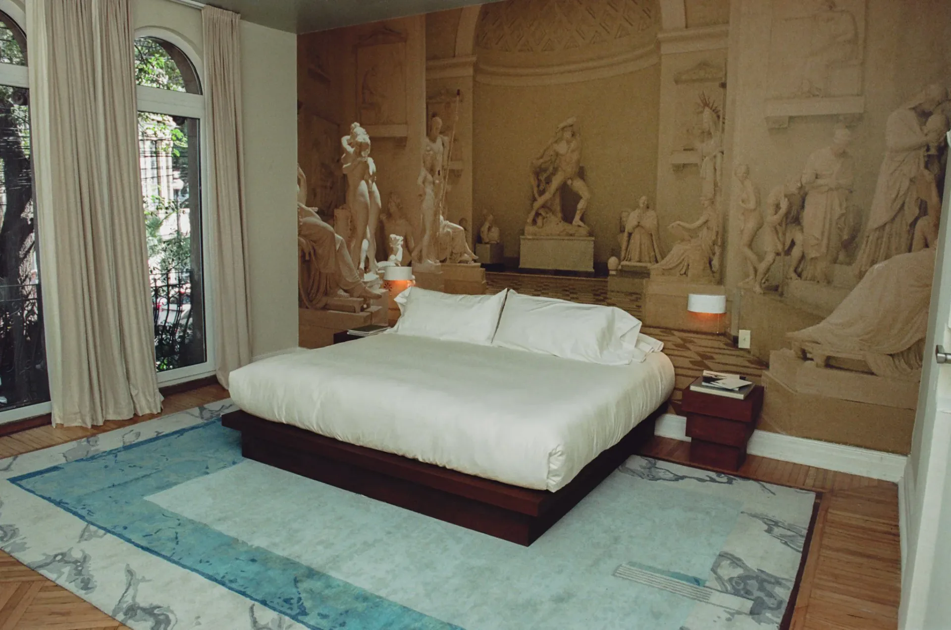Luxurious bedroom with classical marble statuary, cream platform bed, turquoise patterned floor, and arched alcoves by Rafael Prieto.