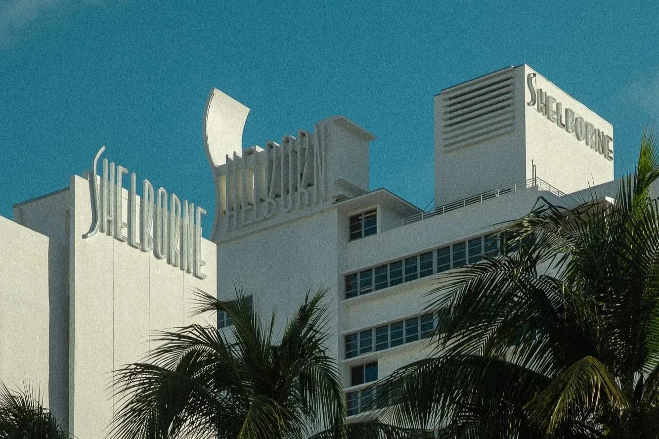 Mid-century modern commercial building with white facade and prominent signage featuring palm trees against blue sky, designed by Rafael Prieto.