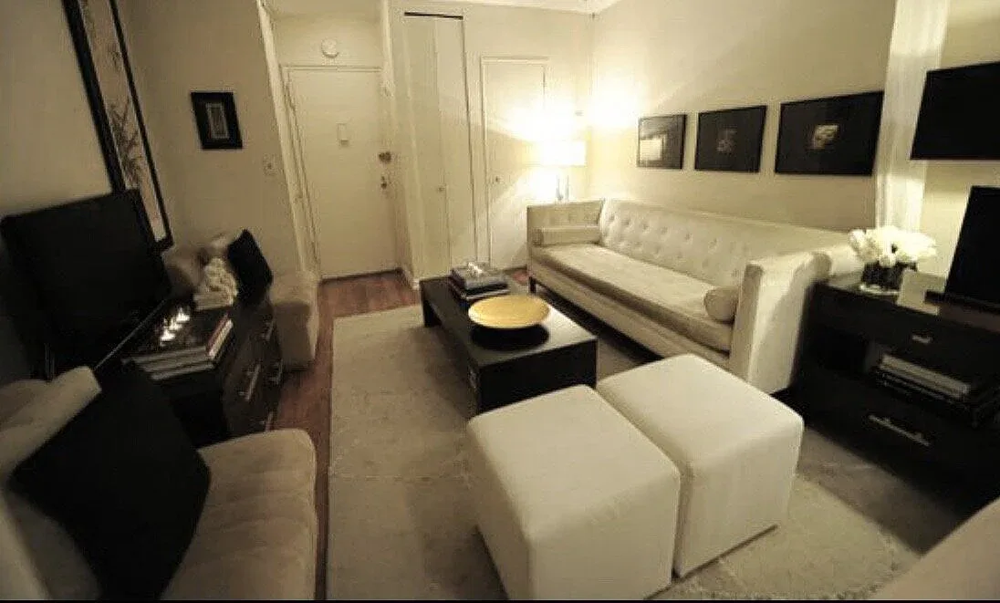 Modern living room with cream sofa, white cube ottomans, black entertainment console, and neutral palette by Rahbia Allen.