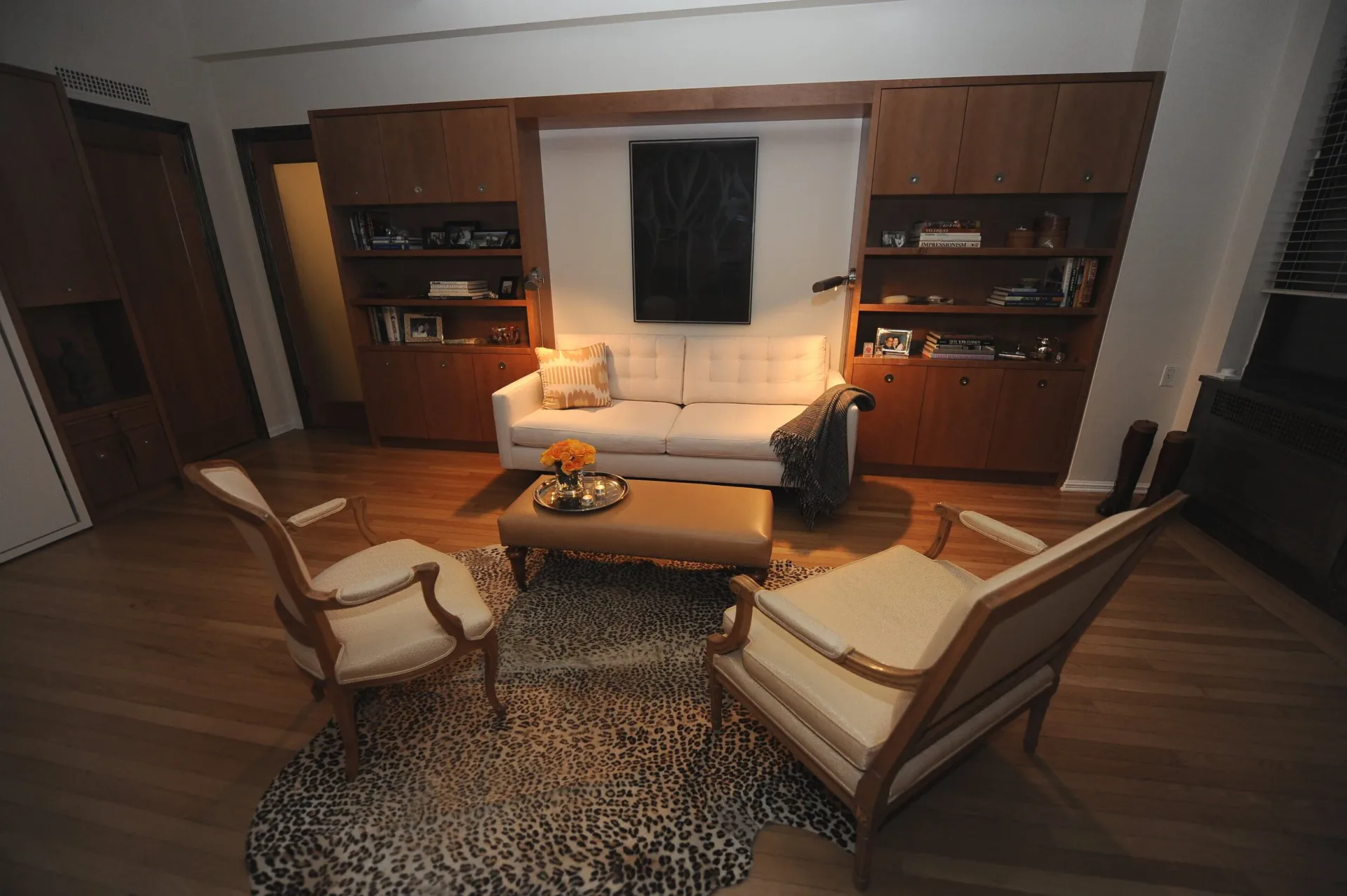 Mid-century modern living room with warm wood paneling, cream upholstered seating, leopard-print area rug, and built-in cabinetry by Rahbia Allen.