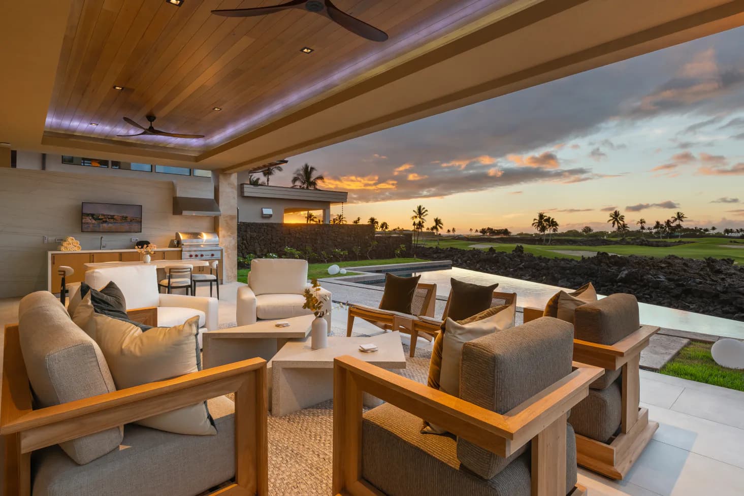 Modern lounge space with wooden ceiling beams, neutral upholstered seating, and expansive windows overlooking a sunset agricultural landscape by Rddhima Golyan.