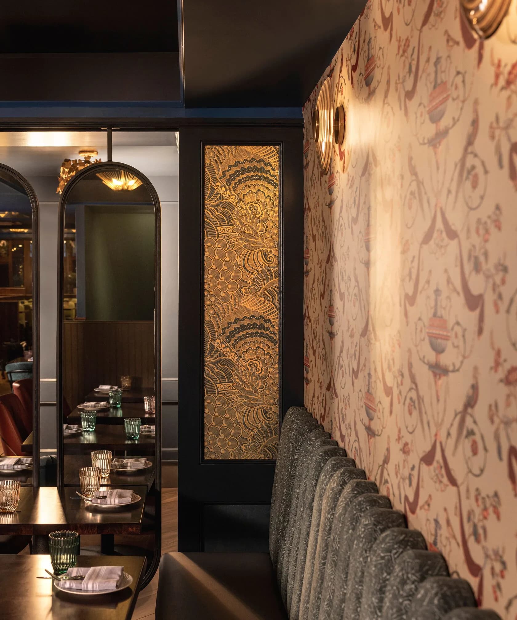 Elegant restaurant interior featuring cream damask wallpaper, arched mirror-fronted wine display, brass decorative panel, and intimate dining setup with warm lighting by Rddhima Golyan.