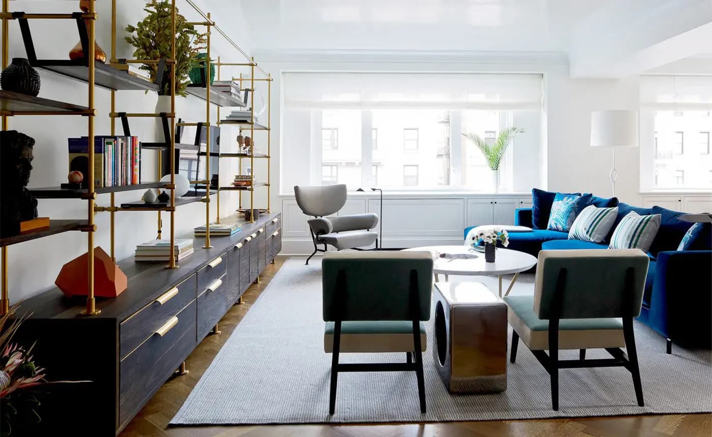 Bright modern living room with blue sectional sofa, black accent chairs, metal shelving unit, and neutral area rug by Rebecca Ascher.
