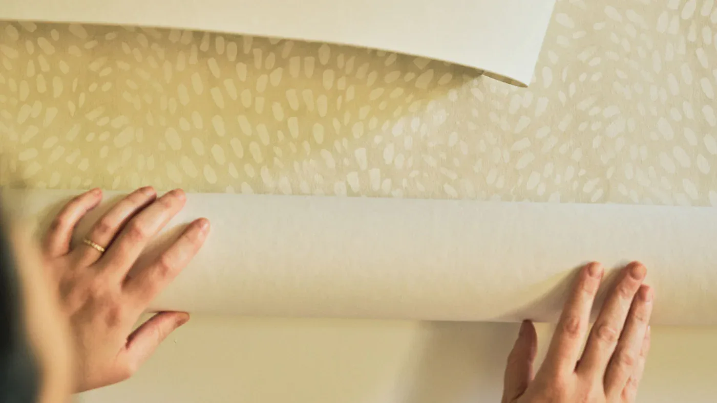 Hands installing textured wallpaper or wall covering in neutral tones, showing material application and installation detail by Rebecca Atwood.