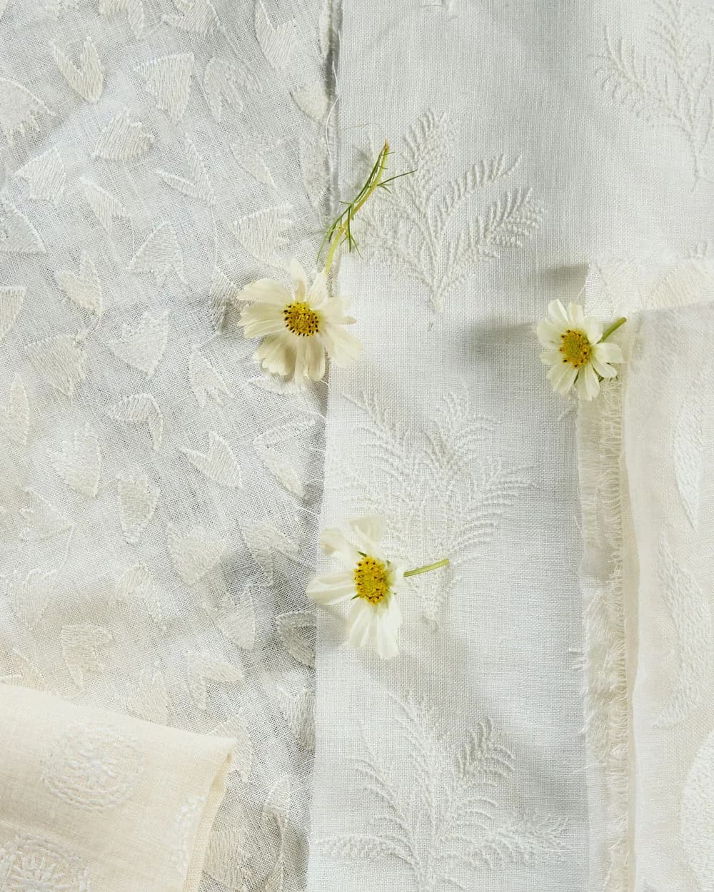 White textured curtain or textile with delicate fern-like pattern details, styled with fresh white daisies with yellow centers by Rebecca Atwood.