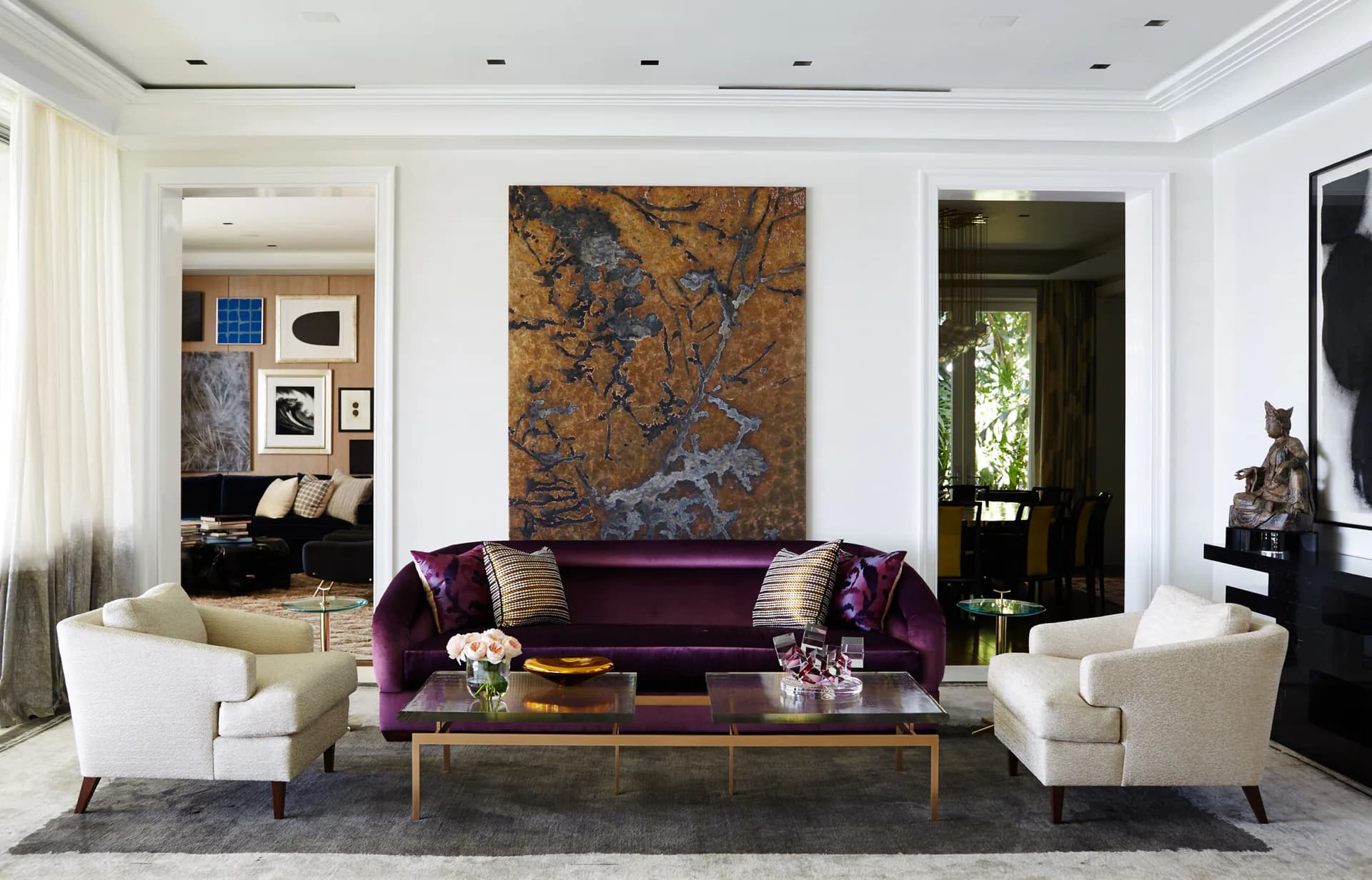 Luxurious living room with plush purple velvet sofa, cream armchairs, gold-framed coffee table, and abstract artwork by Regina Garcia-marin.