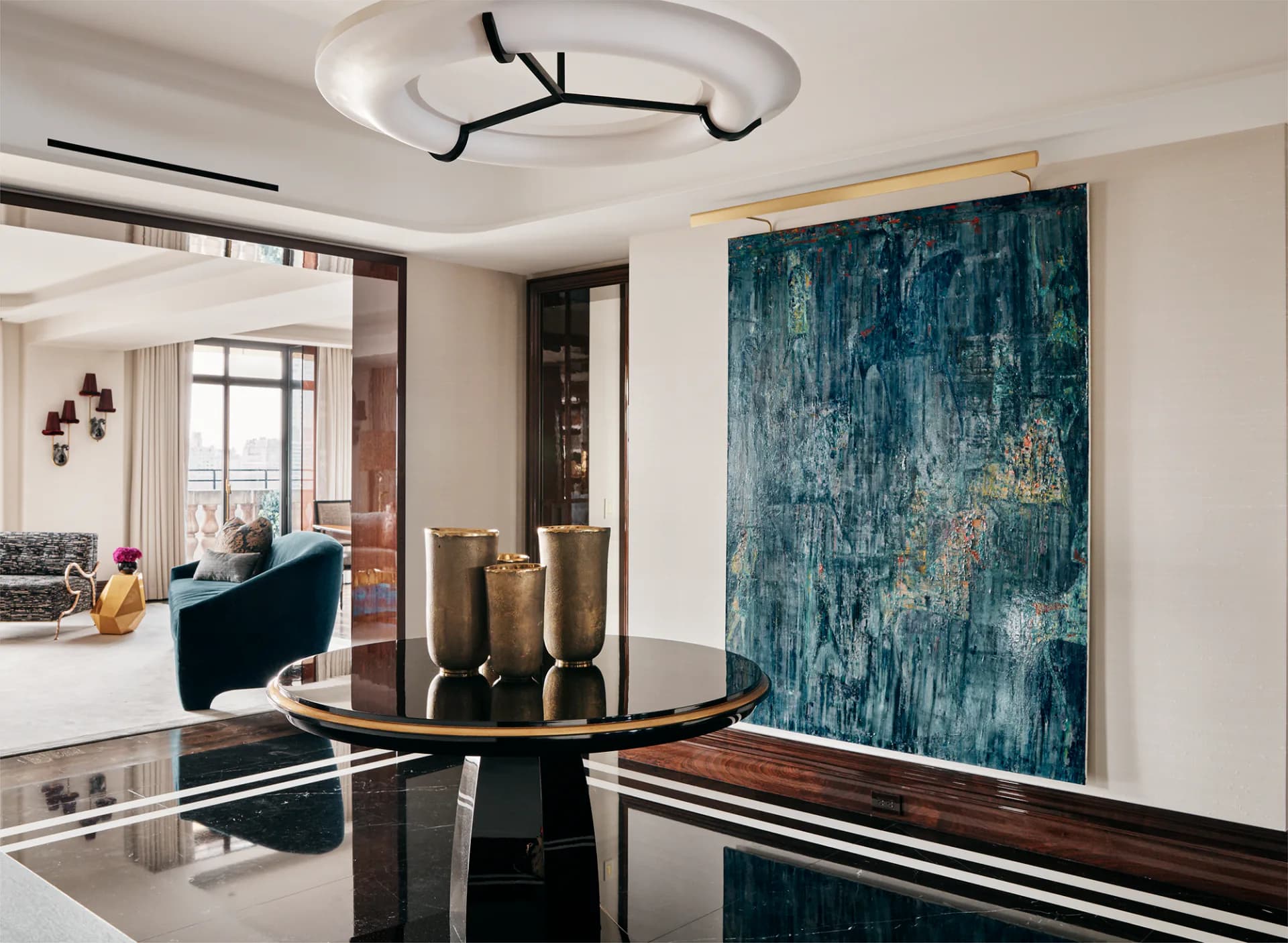 Modern dining room with round black table, teal abstract artwork, brass cylinders, and sculptural ceiling fixture by Regina Garcia-marin.