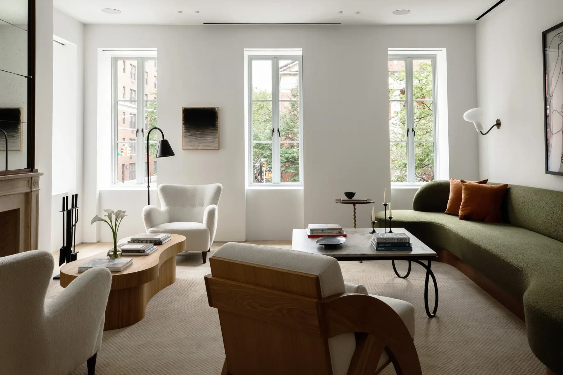 Bright modern living room with green sofa, cream armchairs, wood accents, and tall windows overlooking greenery, designed by Reinaldo Leandro.