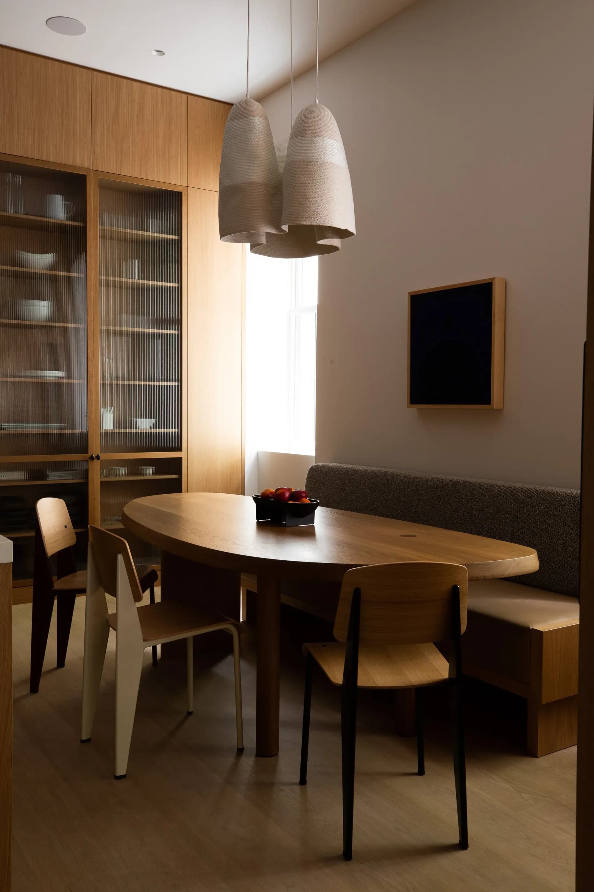 Modern dining room with oval wood table, black chairs, pendant lights, wood cabinetry, and minimalist aesthetic by Reinaldo Leandro.