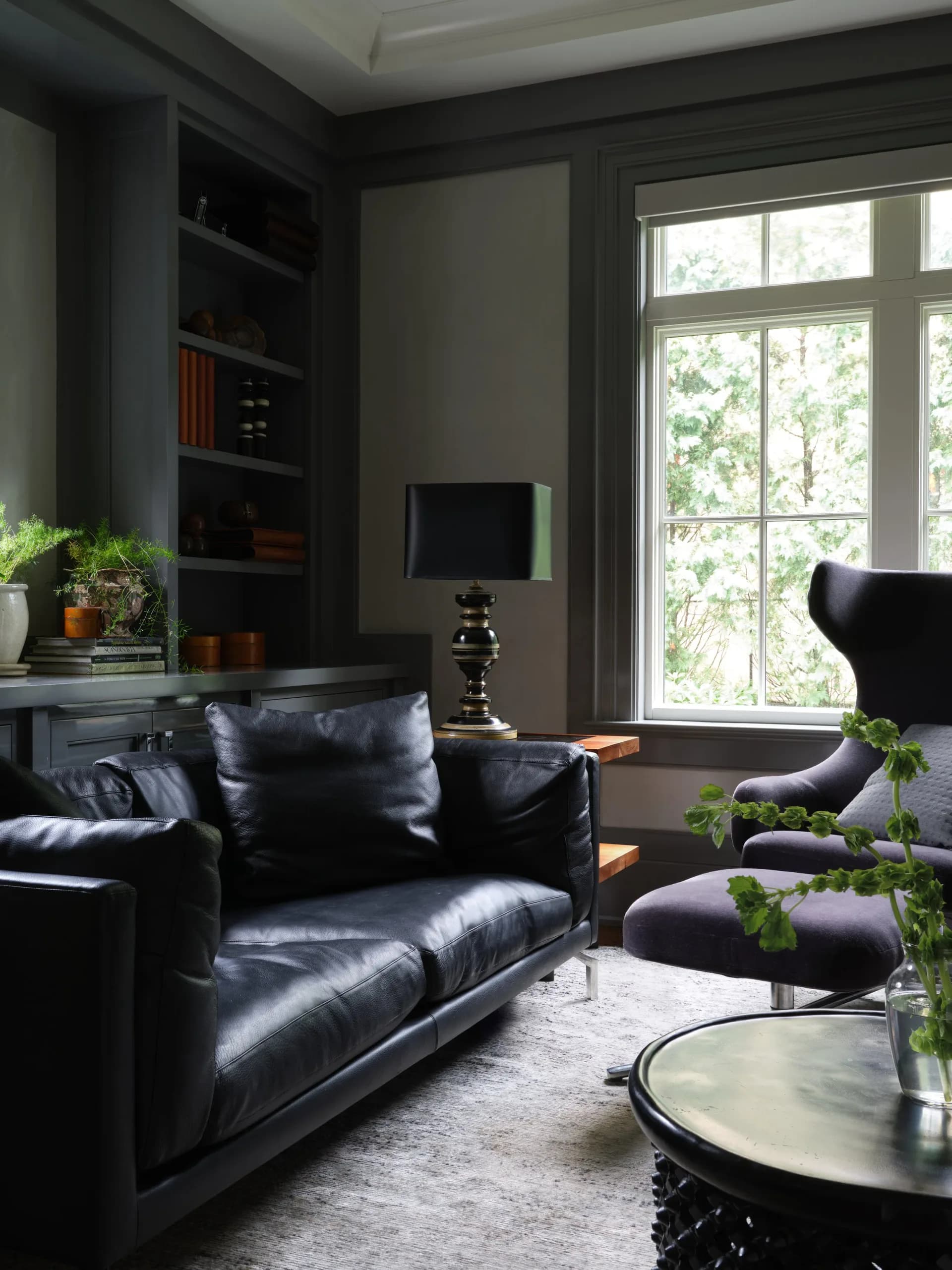 Modern living room with dark charcoal walls, black leather seating, large windows, built-in shelving, and contemporary furnishings by Remi Berger.