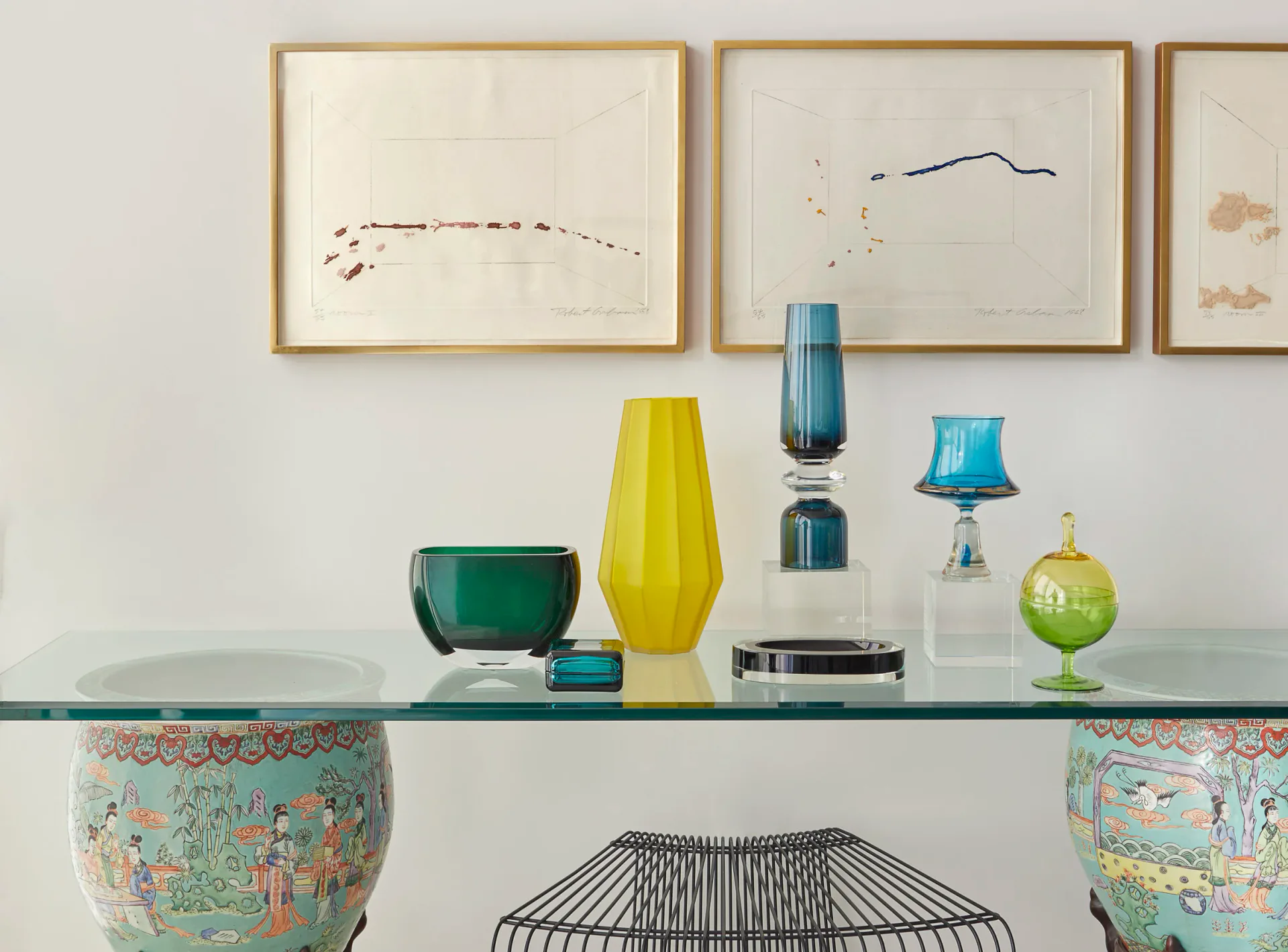 Minimalist shelving display with glass vases, geometric forms, and subtle earth tones, featuring framed abstract artwork above, designed by Remigio Gudin.