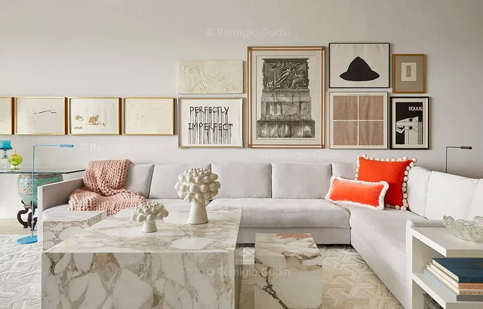 Modern living room with white sectional sofa, marble coffee table, neutral palette, and curated gallery wall of framed artwork above by Remigio Gudin.