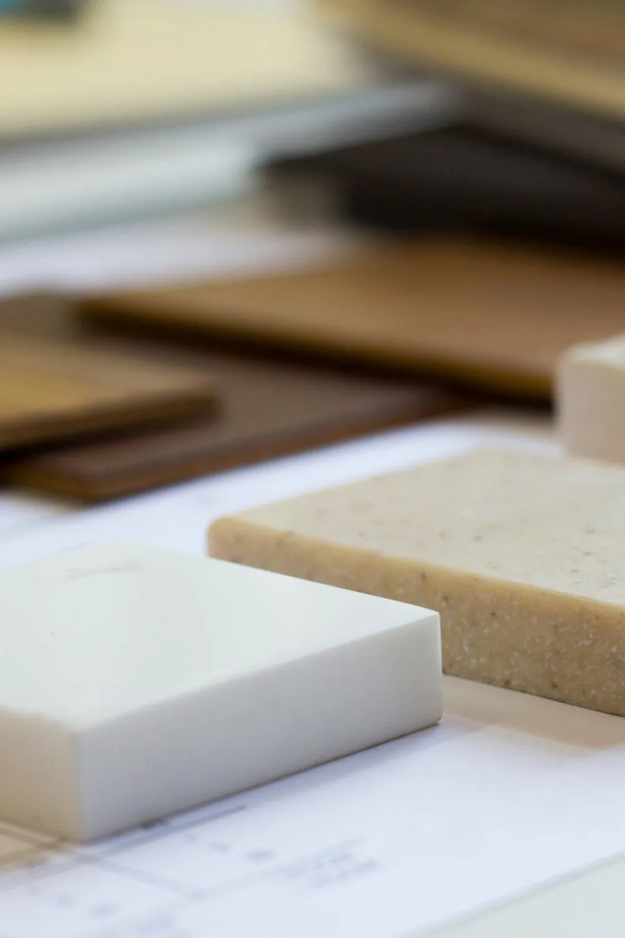 Close-up of material samples including white and tan textured surfaces arranged on a work surface, showcasing design palette materials by Remy Maurice.