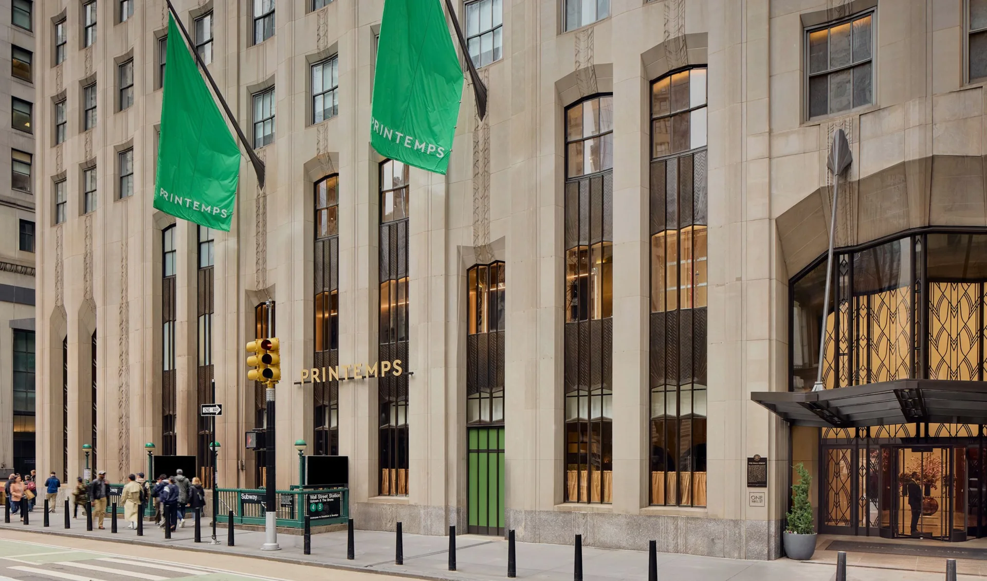 Classical facade with green banners and tall windows showing interior lighting, contemporary storefront design by Reynald Philippe.