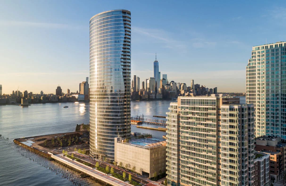 Waterfront luxury residential tower with curved glass facade overlooking Manhattan skyline and East River, designed by Rhea Thomas.