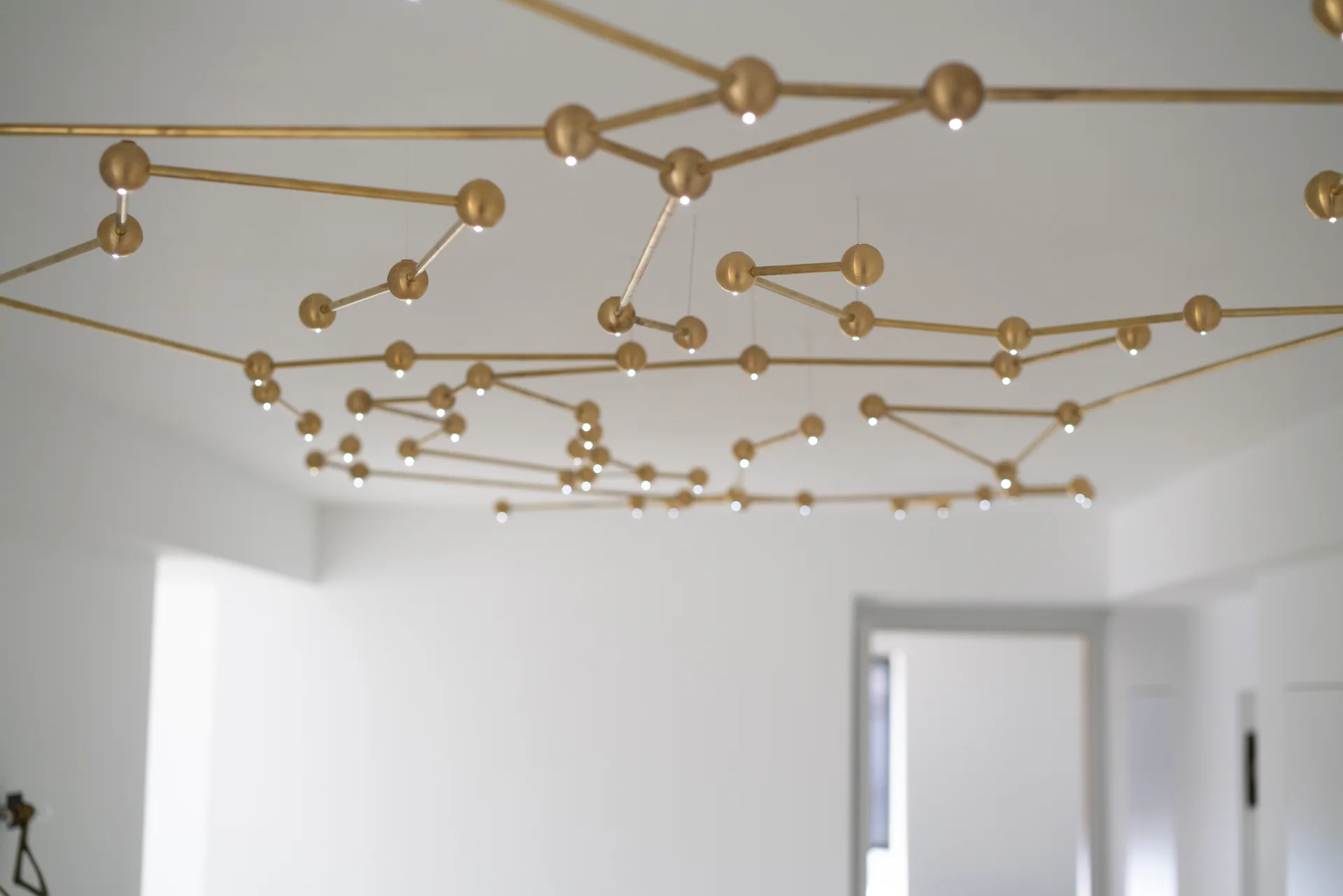 Brass spheres connected by linear rods form an abstract sculptural ceiling installation in a minimalist white interior by Richard Clarkson.