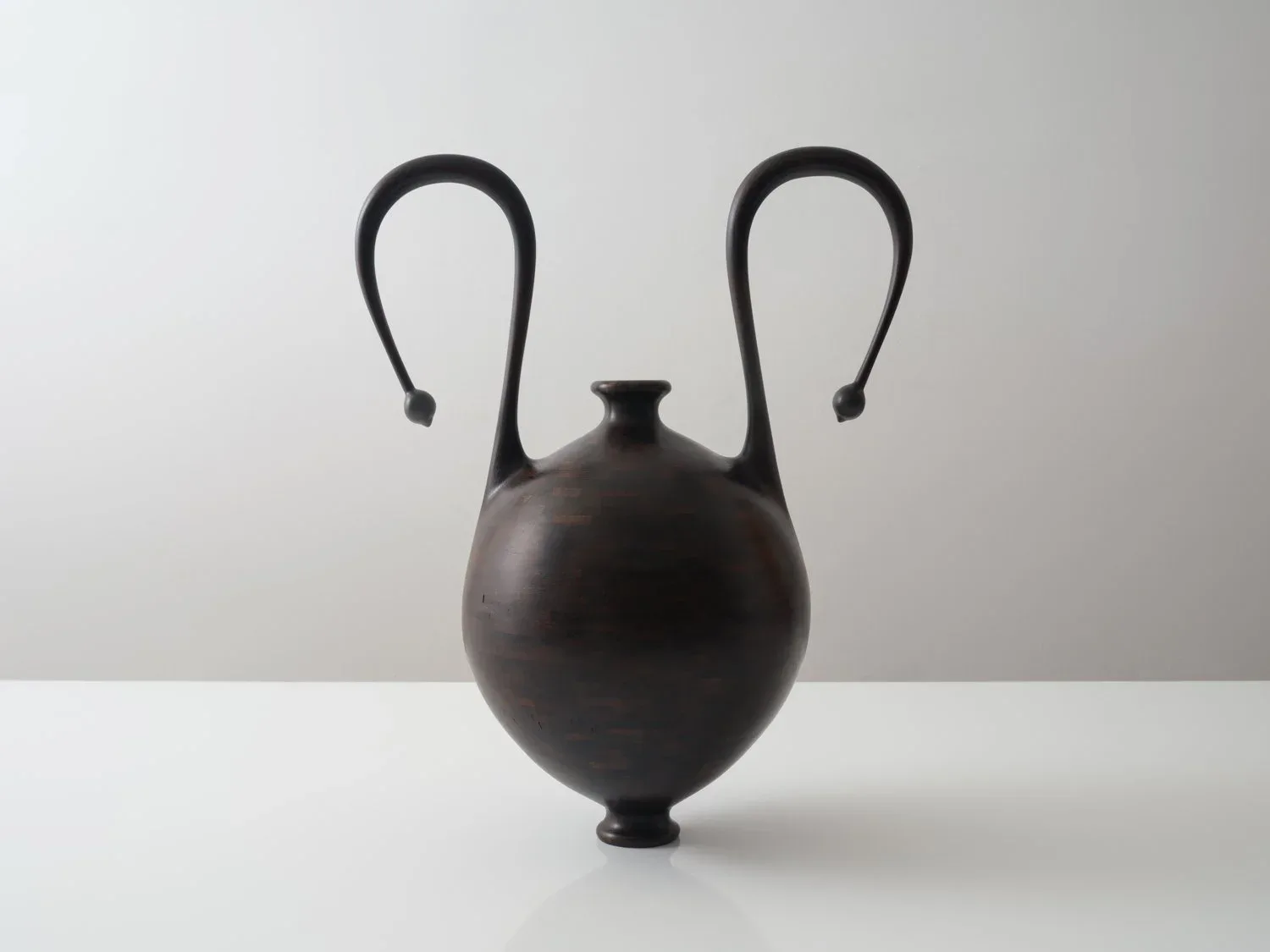 Dark spherical ceramic vessel with curved black handles extending upward, minimalist sculptural form by Richard Haining.