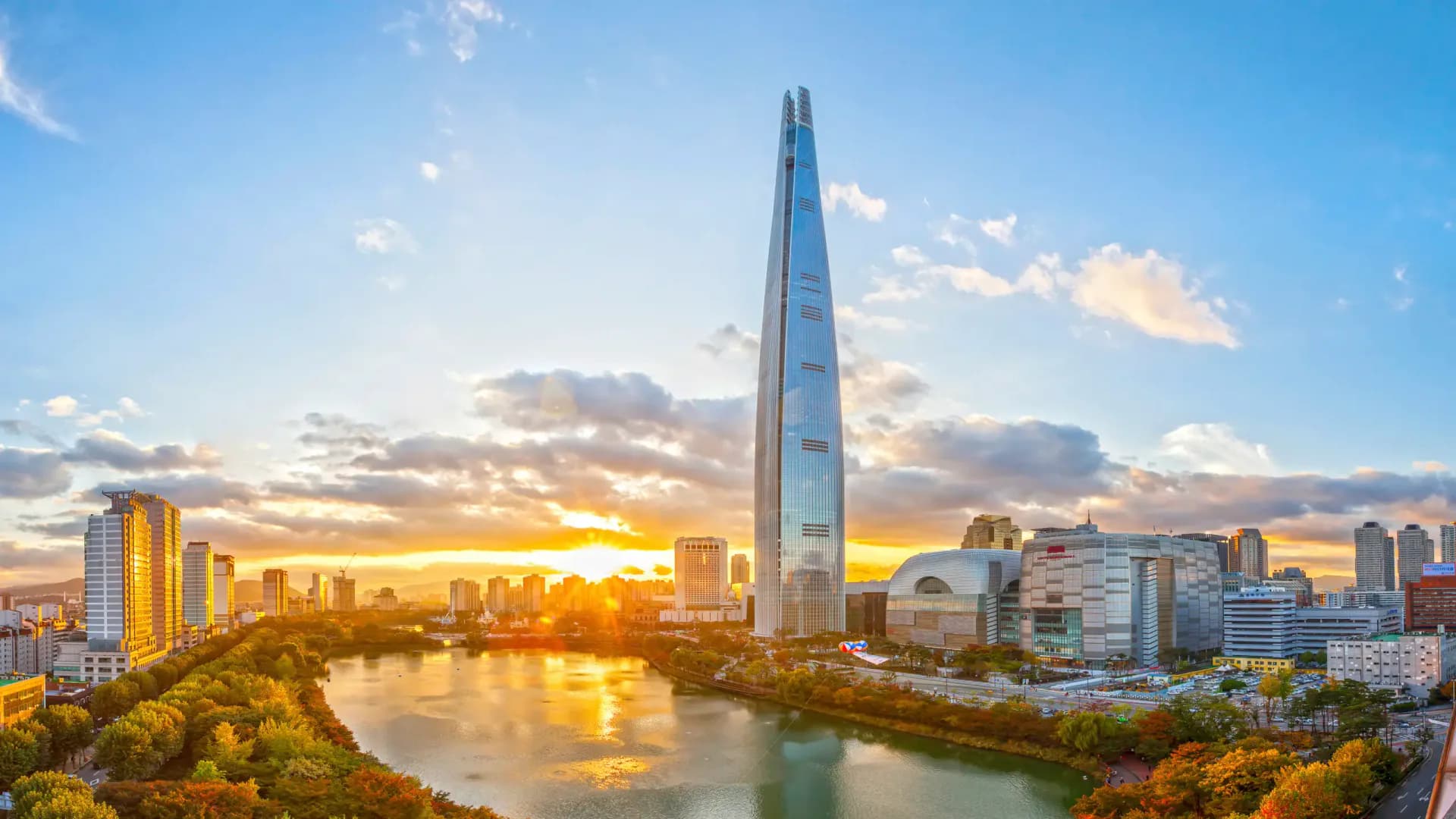 Seoul skyline at sunset featuring the Lotte World Tower reflected in the Han River, with golden hour lighting and autumn foliage by Richard Nemeth.