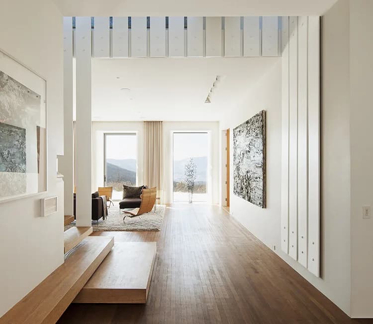 Modern minimalist hallway with white walls, light wood flooring, and floor-to-ceiling windows overlooking mountains, designed by Rick Cook.