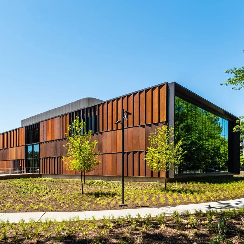 Modern building with oxidized copper and black metal cladding, featuring large windows and integrated landscaping, designed by Rick Cook.