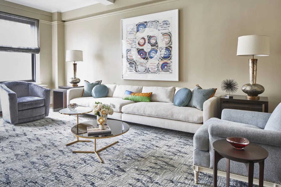 Sophisticated living room with neutral palette, cream sofa, blue armchairs, geometric area rug, and blue abstract artwork by Rinat Lavi.