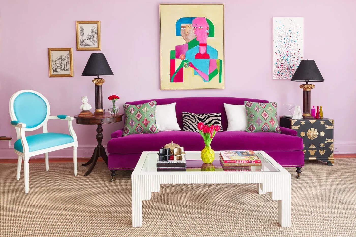 Colorful living room with magenta sofa, turquoise accent chair, white coffee table, and vibrant artwork against pink walls, designed by Ritika Bhasin.