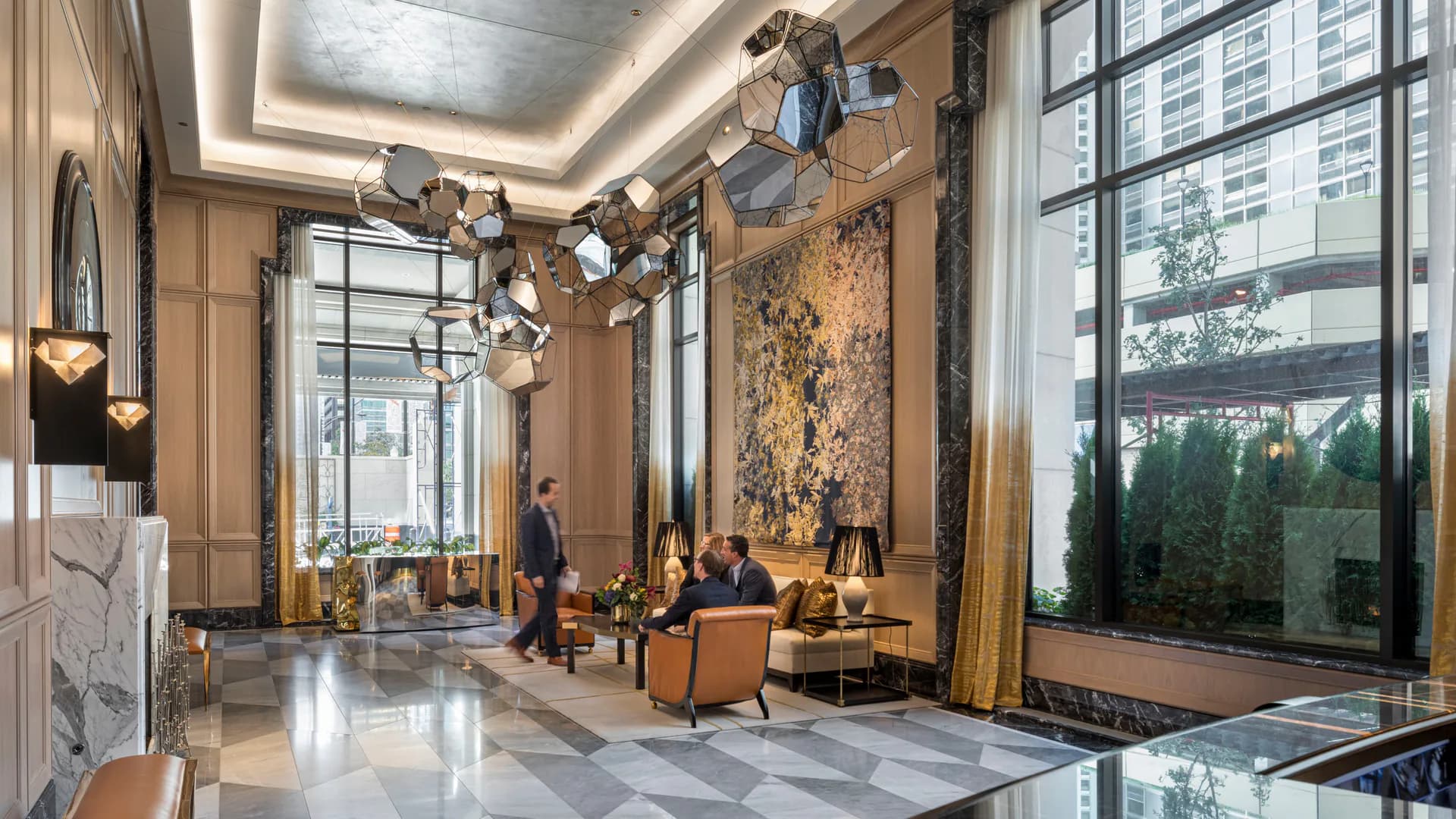 Luxurious hotel lobby featuring warm tan walls, polished marble flooring, sculptural ceiling installations, and floor-to-ceiling windows overlooking the city, designed by Robert A.M. Stern.