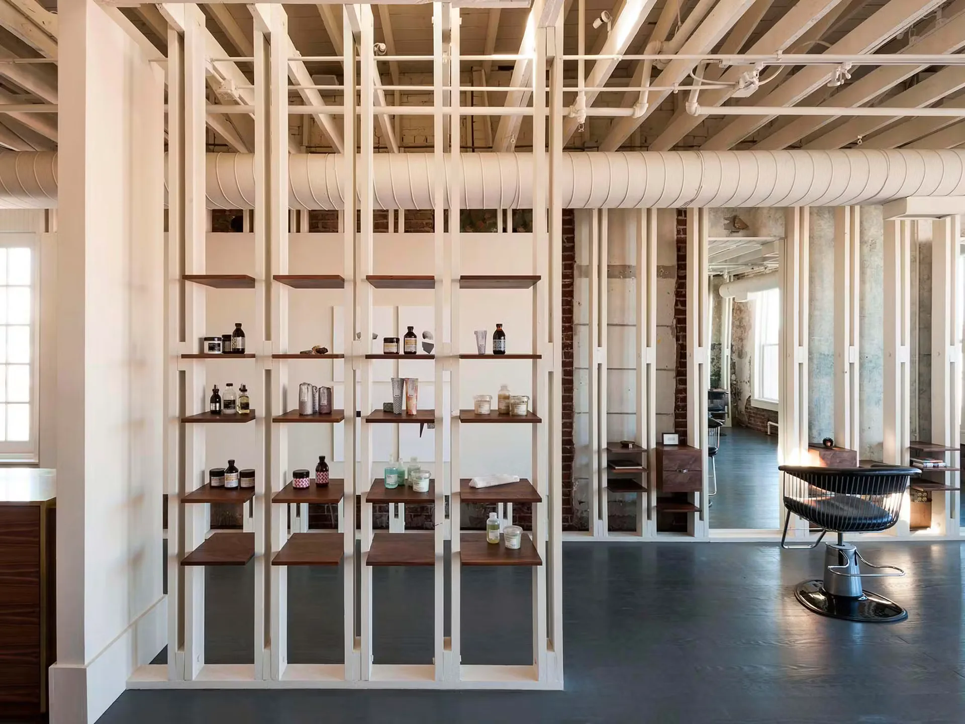 Modern loft interior with white steel shelving unit displaying objects, polished concrete floors, and glass-partitioned spaces beyond, designed by Robert Highsmith.