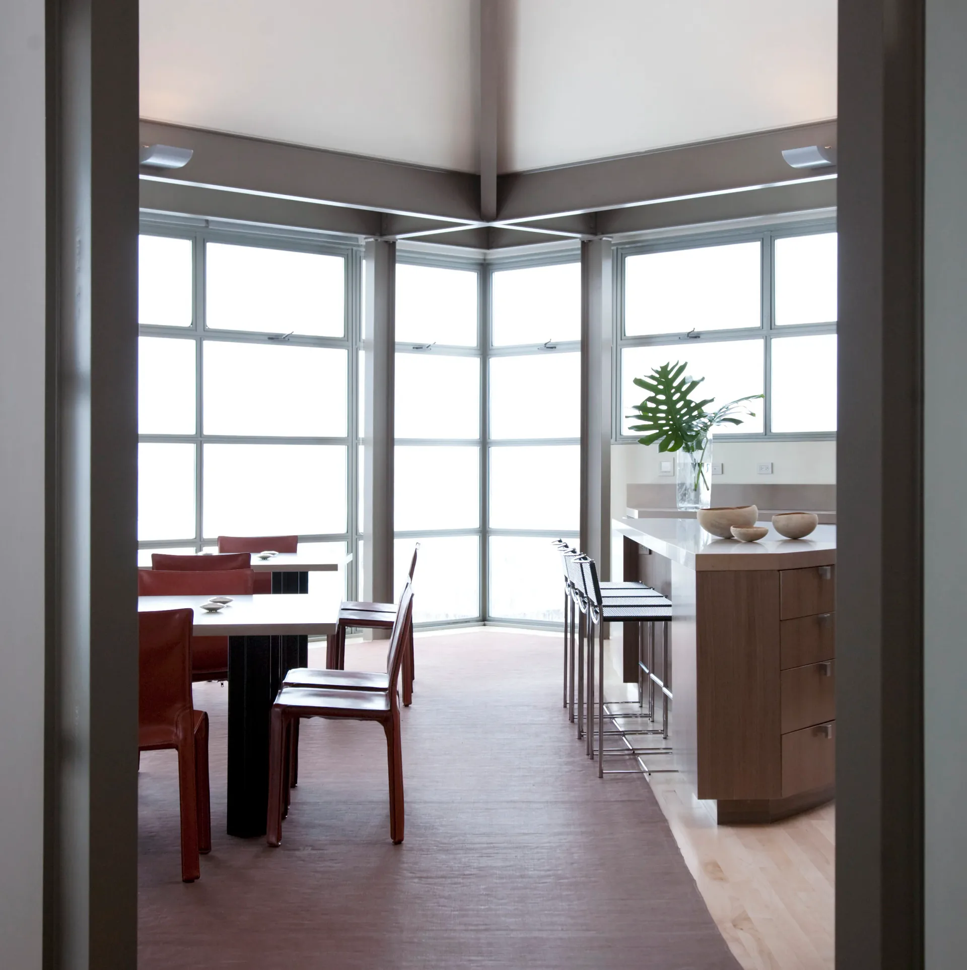 Modern dining and kitchen space with floor-to-ceiling windows, dark wood furniture, white cabinetry, and minimalist aesthetic by Robert Nassar.