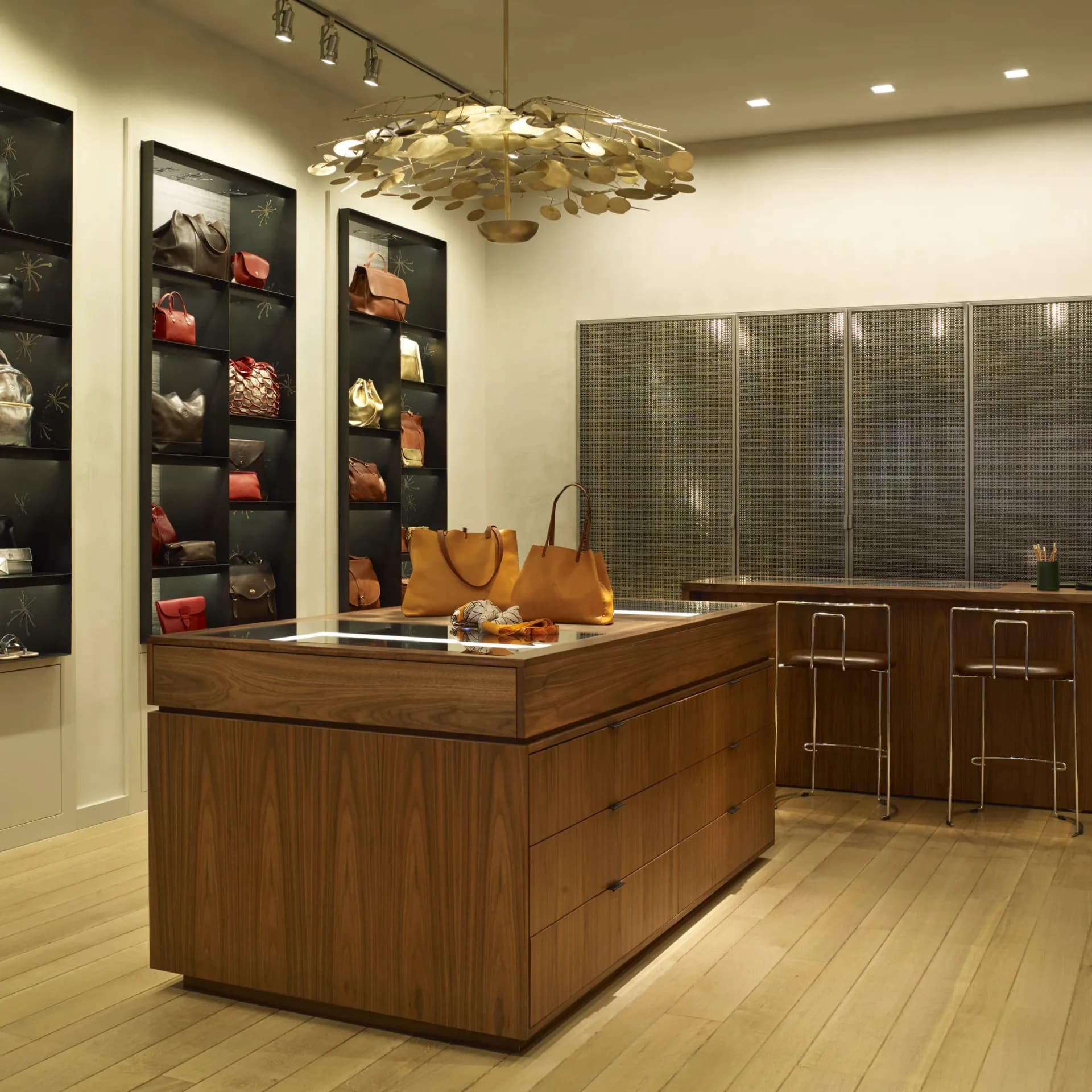 Modern retail interior with wooden display island, wall-mounted shelving with products, golden leaf pendant light, and neutral palette by Robert Nassar.