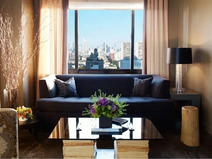 Modern luxury living room with dark navy sofa, glass coffee table, and floor-to-ceiling windows overlooking a city skyline, designed by Robert Rice.