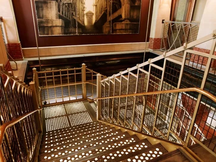 Interior view of a modern stairwell with wooden and white metal railings, polka-dot patterned flooring, and warm-toned architectural elements by Robert Rice.