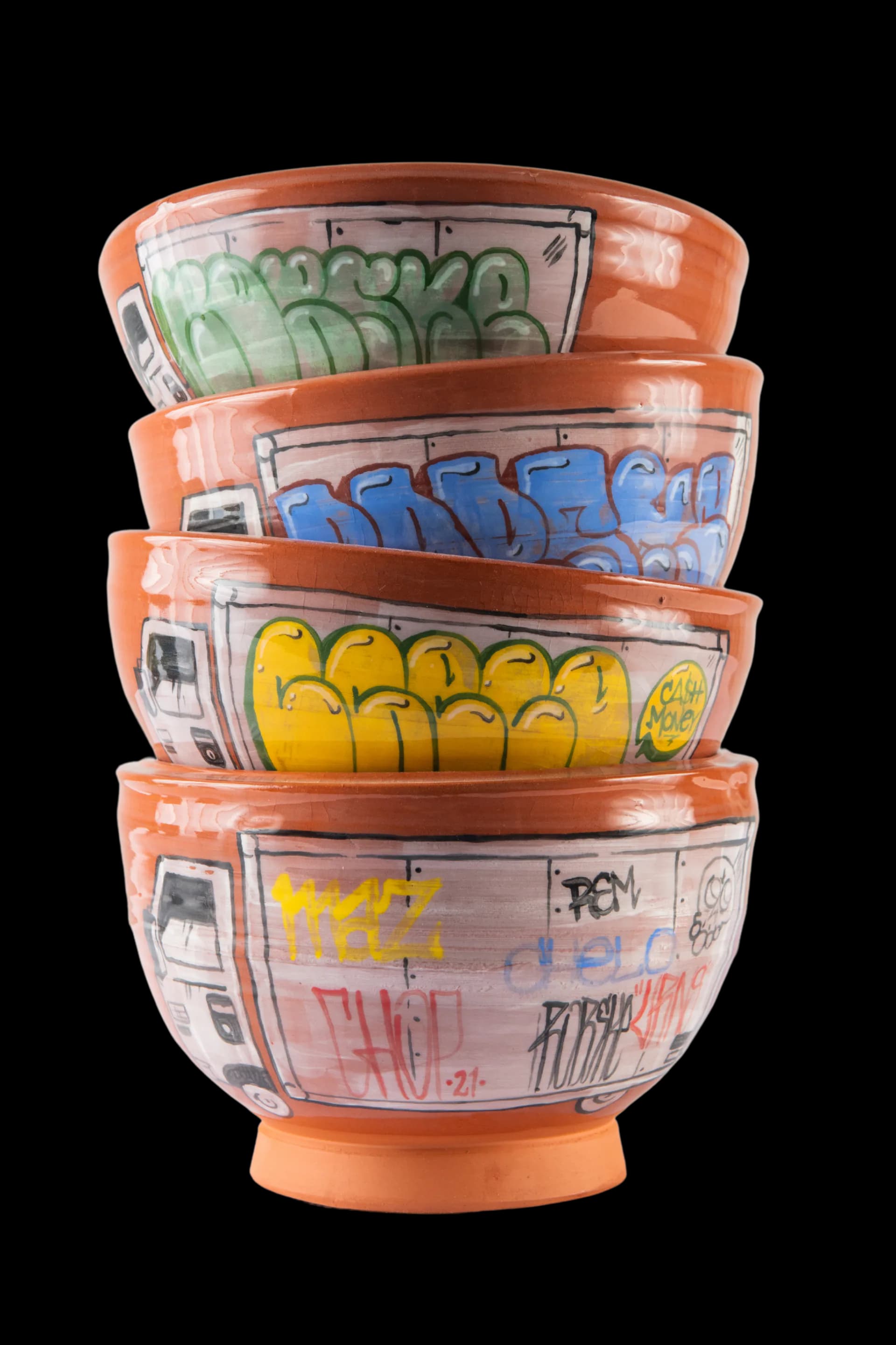 Stacked orange ceramic bowls with graffiti-style artwork in green, blue, and yellow, designed by Roberto Lugo.