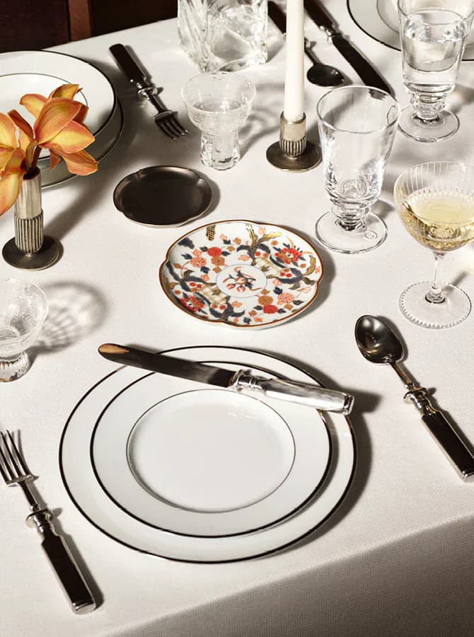 Elegant formal place setting with white plates rimmed in black, decorative patterned bread plate, black flatware, and crystal glassware on white tablecloth by Robin Standefer.